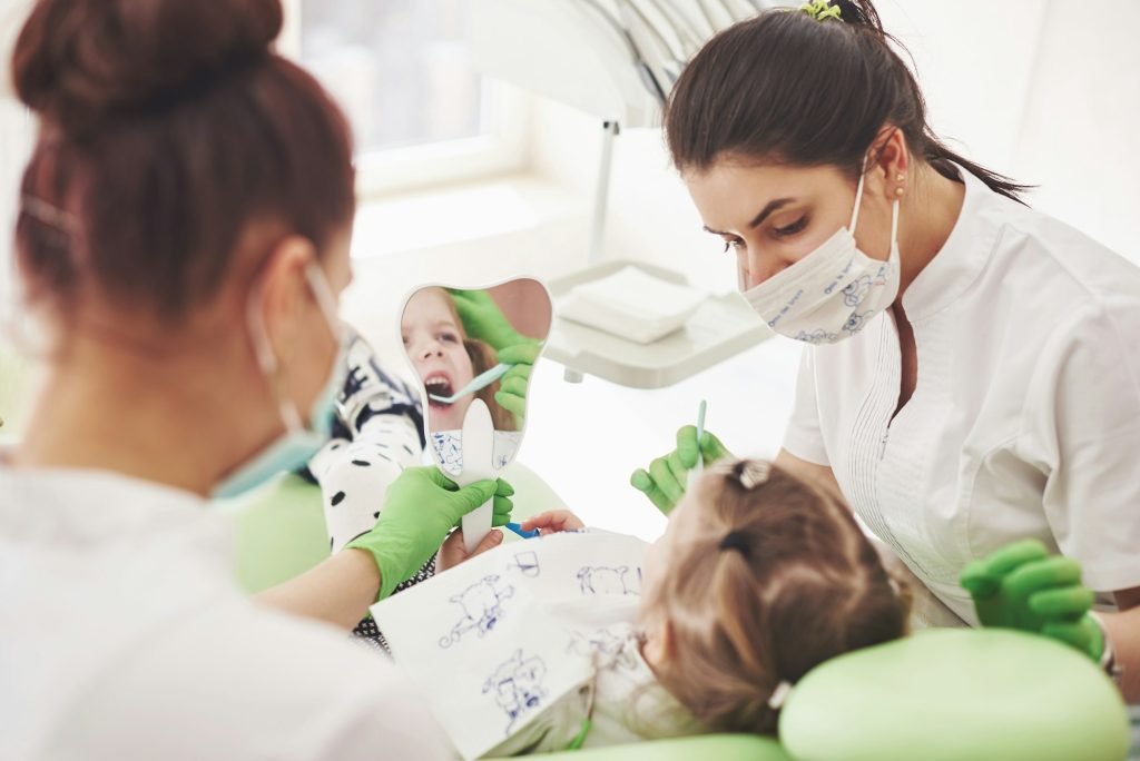 pediatric dentist and assistant making examination procedure for smiling cute little girl