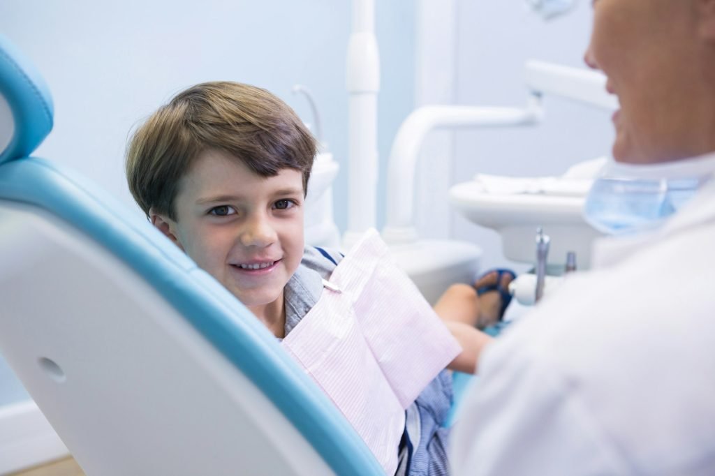 Portrait of cute boy sitting on dentist chair by dentist